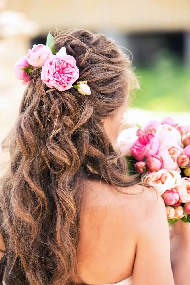 Frau mit gelocktem langen Haar mit rosanen Blüten und Blumenstrauß